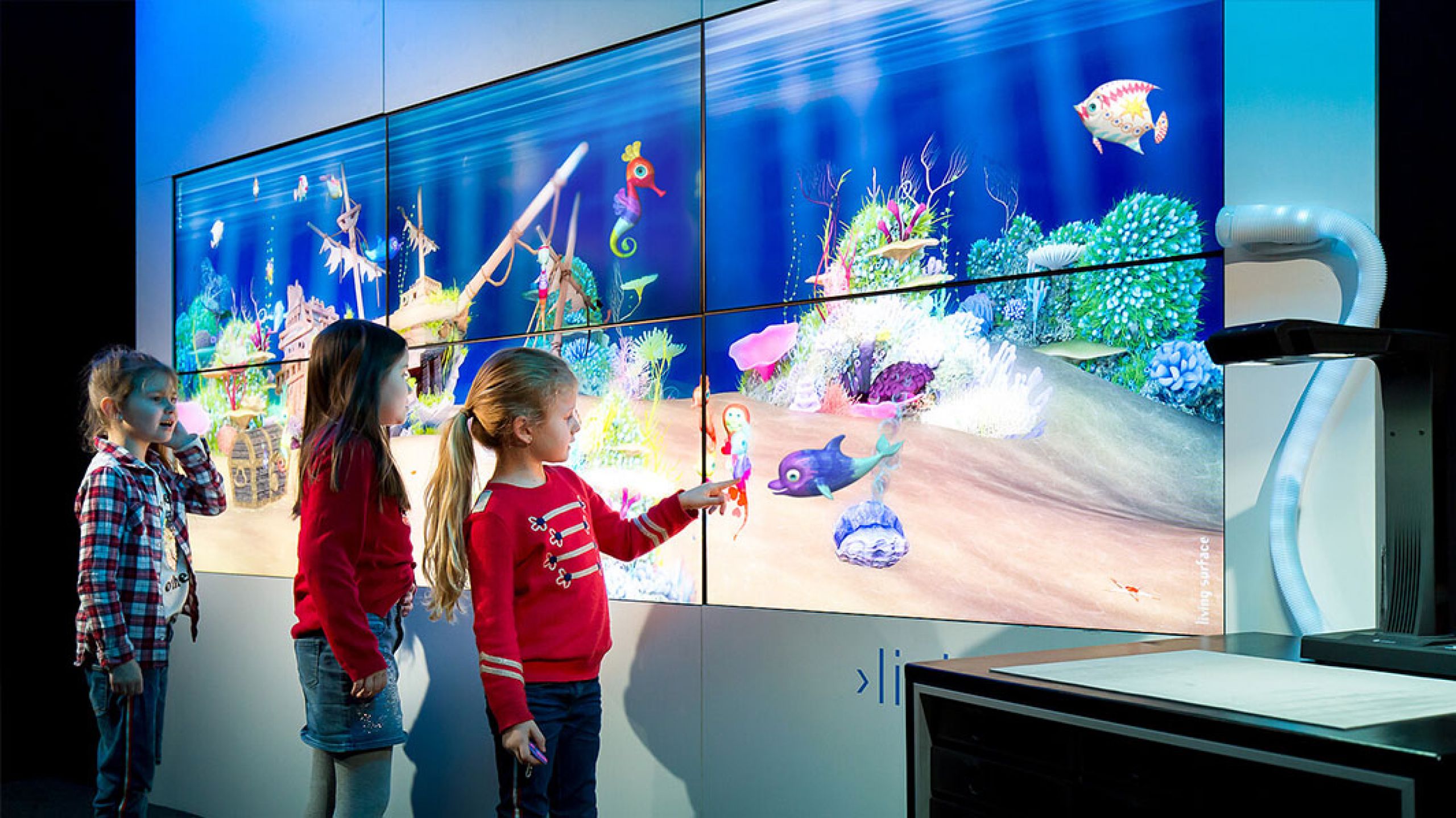 Zwei Mädchen entdecken ihre gemalten Fische im paint2life Aquarium