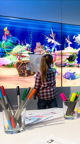 Ein Mädchen steht vor dem paint2life Aquarium und beobachtet ihren gemalten Fisch